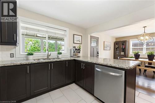 Kitchen featuring dark cabinetry, speckled stone countertops, a stainless steel dishwasher, and a double basin sink beneath a large window - 60 Avenue Road, Cambridge, ON - Indoor Photo Showing Kitchen
