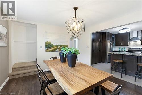 Open-concept dining area featuring wood-finish flooring, a contemporary geometric chandelier, and a built-in kitchen island with seating - 60 Avenue Road, Cambridge, ON - Indoor Photo Showing Dining Room