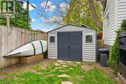 Compact backyard featuring a gray storage shed with double doors and window accents, perimeter wood fencing, and a stone paver path - 60 Avenue Road, Cambridge, ON - Outdoor