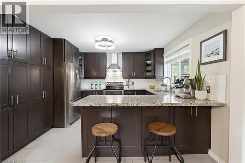 Kitchen featuring dark wood-finish cabinetry, light speckled countertops, a stainless steel refrigerator, and a tiled backsplash - 60 Avenue Road, Cambridge, ON - Indoor Photo Showing Kitchen With Upgraded Kitchen