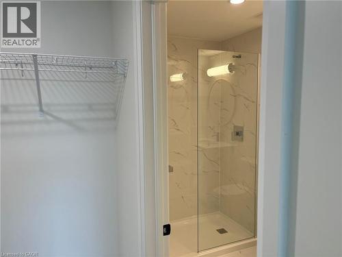 Glass-enclosed shower featuring white-veined wall tile, a built-in shower shelf, and a square drain - 3370 Stella Crescent Unit# 235, Windsor, ON - Indoor Photo Showing Bathroom