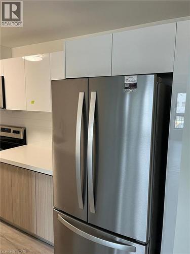 Stainless steel French door refrigerator set against white upper cabinetry and wood-finish lower cabinetry - 3370 Stella Crescent Unit# 235, Windsor, ON - Indoor Photo Showing Kitchen