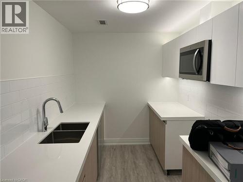 Modern kitchen featuring white flat-panel cabinetry, light wood-finish lower cabinets, white subway tile backsplash, and light-colored countertops - 3370 Stella Crescent Unit# 235, Windsor, ON - Indoor Photo Showing Kitchen With Double Sink
