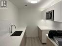 Modern kitchen featuring white flat-panel cabinetry, light wood-finish lower cabinets, white subway tile backsplash, and light-colored countertops - 3370 Stella Crescent Unit# 235, Windsor, ON  - Indoor Photo Showing Kitchen With Double Sink 