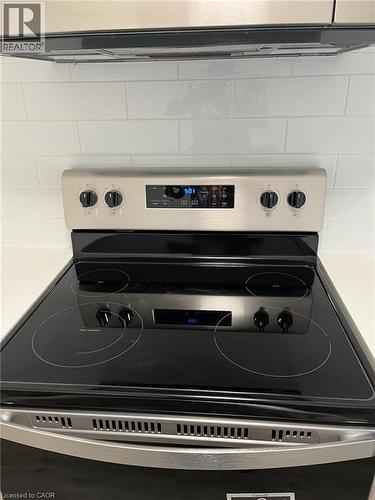 Stainless steel range with a black ceramic glass cooktop, coordinating hood vent, and white subway tile backsplash - 3370 Stella Crescent Unit# 235, Windsor, ON - Indoor Photo Showing Kitchen