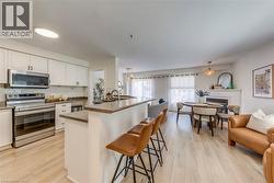 Kitchen and dining area featuring light wood-finish flooring, white cabinetry with dark pulls, stainless steel appliances, and a breakfast bar with a sink - 