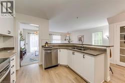 Kitchen featuring white cabinetry, stainless steel appliances, a double basin sink, and wood-finish flooring - 
