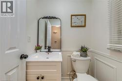 Powder room featuring wainscoting, a wall-mounted vanity with integrated sink, a black-framed mirror, and a white toilet - 