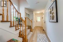 Foyer featuring light wood-finish flooring, staircase with carpeted treads and wood banister, white walls, and a front entry door with decorative glass inserts - 