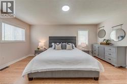 Spacious bedroom featuring light wood-finish flooring, two windows with blinds, a flush mount ceiling light, and ample wall space - 