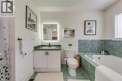 Bathroom featuring a built-in tub with green tiled surround, matching green tile flooring, a single vanity with a white countertop and base cabinetry, a wall-mounted illuminated mirror, and a window w - 