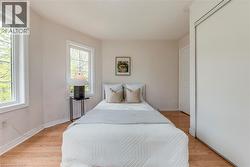 Room featuring wood-finish flooring, two large windows, painted walls, white trim, and a built-in sliding door closet - 