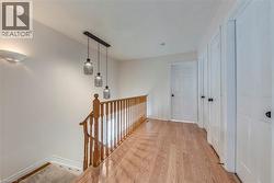 Upper-level hallway featuring wood-finish flooring, a traditional wood railing, a modern linear pendant light fixture with three glass shades, and multiple white panel doors with black hardware - 