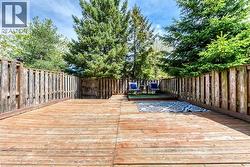 Spacious wood deck featuring a privacy fence, mature trees, and an elevated seating area with artificial turf - 