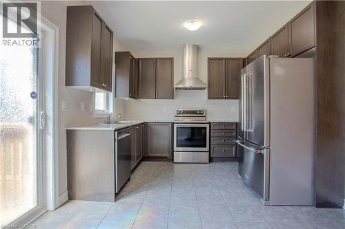 Modern kitchen featuring dark wood-finish cabinetry, stainless steel appliances, light-toned countertops, and a sliding glass door - 3896 Tufgar Crescent, Burlington, ON - Indoor Photo Showing Kitchen With Stainless Steel Kitchen