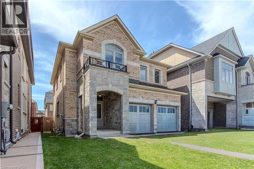 Two-story home featuring a stone and brick exterior, two garage bays with panel doors, an arched stone entryway, a second-story balcony with metal railing, and a side pathway leading to a wooden fence - 3896 Tufgar Crescent, Burlington, ON - Outdoor With Facade