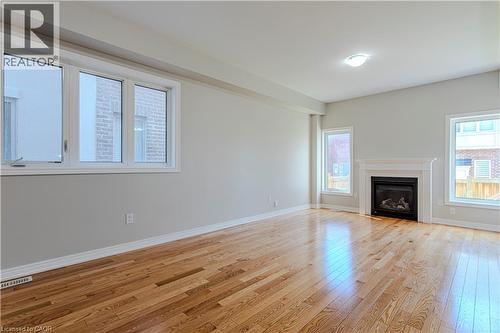 Spacious room featuring wood-finish flooring, a contemporary fireplace with a white mantel, multiple windows, and a ceiling-mounted light fixture - 3896 Tufgar Crescent, Burlington, ON - Indoor Photo Showing Living Room With Fireplace