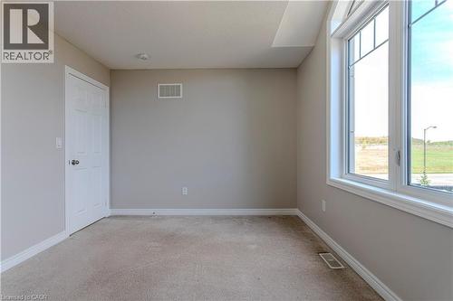 Neutral-toned room featuring a large window with white trim, light beige wall paint, plush carpeting, a white paneled door, and ceiling-mounted lighting - 3896 Tufgar Crescent, Burlington, ON - Indoor Photo Showing Other Room