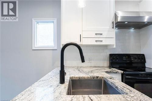 Kitchen view of electric range, tasteful backsplash, white cabinetry, and light stone countertops - 222 Kensington Avenue N, Hamilton, ON - Indoor Photo Showing Kitchen