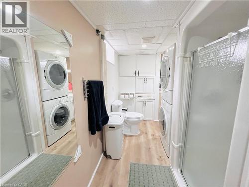 Full bathroom featuring a shower stall with clear glass, wood-finish flooring, and a white toilet - 56 Eastvale Place, Hamilton, ON - Indoor Photo Showing Laundry Room