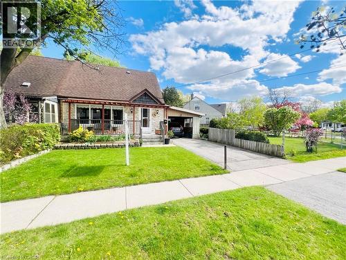 Stone-front home featuring a covered front porch with dark railings, a paved driveway, and an attached carport - 56 Eastvale Place, Hamilton, ON - Outdoor