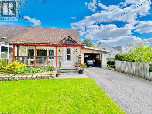 Stone facade residence featuring a covered front porch with a wood pergola, a front lawn, and a paved driveway leading to a carport - 56 Eastvale Place, Hamilton, ON - Outdoor With Deck Patio Veranda