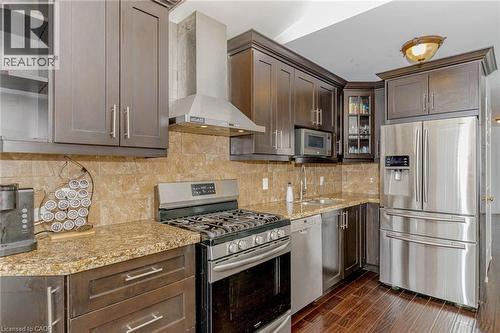 Kitchen with stainless steel appliances, glass insert cabinets, light stone countertops, dark wood finish cabinetry, and decorative backsplash - 32 Vineberg Drive, Hamilton, ON - Indoor Photo Showing Kitchen With Upgraded Kitchen