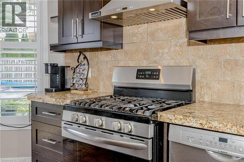 Kitchen with stainless steel appliances, dark wood finish cabinets, backsplash, and light stone countertops - 32 Vineberg Drive, Hamilton, ON - Indoor Photo Showing Kitchen