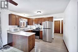 Kitchen featuring wood-finish cabinetry, light-toned countertops, and stainless steel appliances including a refrigerator and range - 