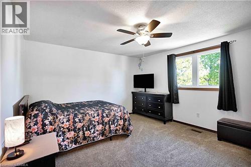 Carpeted room featuring a ceiling fan with integrated lighting, a double window with wood trim, and freshly painted white walls - 16 Sandlewood Avenue, Brantford, ON - Indoor Photo Showing Bedroom