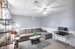 Finished room featuring light-toned walls with wainscoting, wood-finish flooring, a drop ceiling, and a ceiling fan with integrated lighting - 