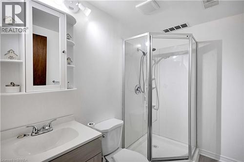 Contemporary bathroom featuring a corner shower with glass enclosure, white vanity with integrated sink, chrome faucet, and mirrored medicine cabinet with open shelving - 16 Sandlewood Avenue, Brantford, ON - Indoor Photo Showing Bathroom