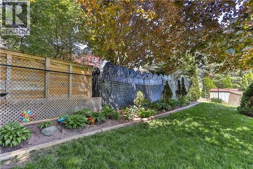 Expansive rear yard featuring a manicured lawn, established garden beds with retaining borders, a decorative masonry wall, mature trees, and a combination wood and chain-link fence - 16 Sandlewood Avenue, Brantford, ON - Outdoor With Deck Patio Veranda