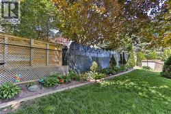 Expansive rear yard featuring a manicured lawn, established garden beds with retaining borders, a decorative masonry wall, mature trees, and a combination wood and chain-link fence - 