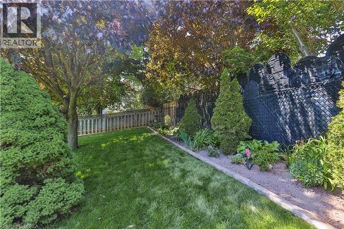 Grassy backyard area featuring mature trees, a planted garden bed, a decorative black fence element, and a light-toned privacy fence - 16 Sandlewood Avenue, Brantford, ON - Outdoor