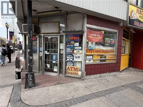 Corner commercial storefront featuring prominent window displays, a red tiled facade, and a glass entrance door - 1 King Street E, Hamilton, ON 