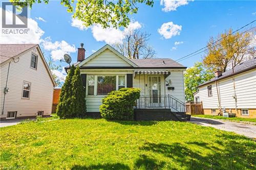 Single-story residence featuring white siding, a dark roof, and a brick chimney - 242 East 43Rd Street, Hamilton, ON 
