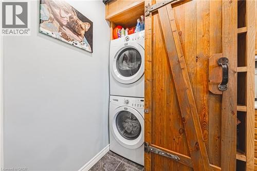 Stacked laundry appliances with overhead shelving, barn door hardware, wood-finish door, light gray walls, and dark flooring - 242 East 43Rd Street, Hamilton, ON - Indoor Photo Showing Laundry Room