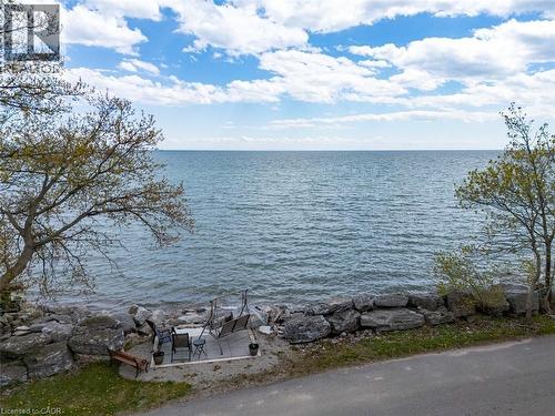 Waterfront property featuring a private stone-lined shore, an outdoor patio, and mature trees providing natural shade - 1395 Lakeshore Road, Haldimand County, ON - Outdoor