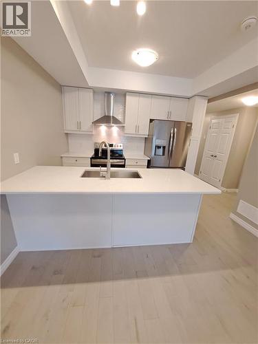 Modern kitchen featuring a large island with an undermount sink, light wood-finish flooring, white cabinetry, stainless steel appliances, and a tiled backsplash - 26 Wheat Lane, Kitchener, ON - Indoor Photo Showing Kitchen