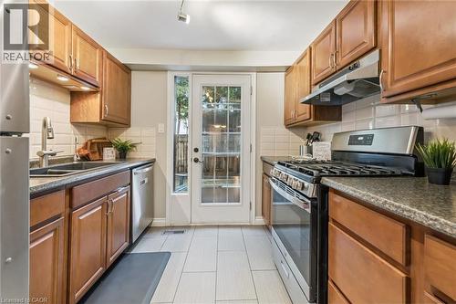 Galley kitchen featuring wood cabinetry, stainless steel appliances, light tile flooring, dark countertops, and a full-light door - 460 Parkview Crescent, Cambridge, ON - Indoor Photo Showing Kitchen With Double Sink