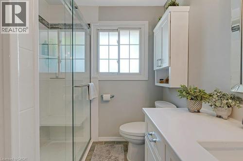 Glass-enclosed shower with a built-in bench, white vanity with an integrated sink, white upper cabinetry, and a grid-patterned window - 236 Winston Boulevard, Cambridge, ON - Indoor Photo Showing Bathroom