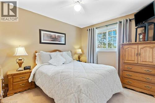 Neutral tone wall paint, flush mount ceiling fan, window with exterior foliage, carpeted flooring, and a decorative picture frame - 236 Winston Boulevard, Cambridge, ON - Indoor Photo Showing Bedroom
