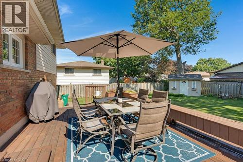 Expansive composite deck featuring multiple seating zones anchored by a dining table with integrated umbrella, geometric patterned outdoor rug, lounge chairs, and a built-in grill - 236 Winston Boulevard, Cambridge, ON - Outdoor With Deck Patio Veranda