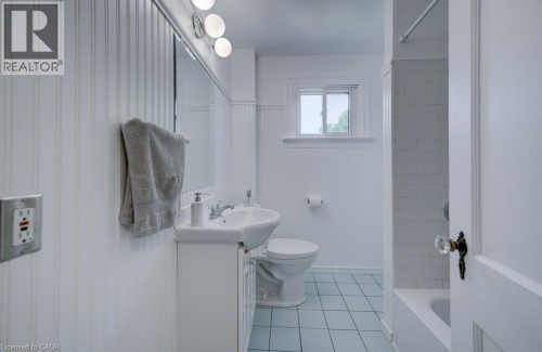 Bathroom featuring a pedestal sink, white beadboard wainscoting, light blue tile flooring, a window, and a bathtub with white subway tile surround - 209 Belleview Avenue, Kitchener, ON - Indoor Photo Showing Bathroom