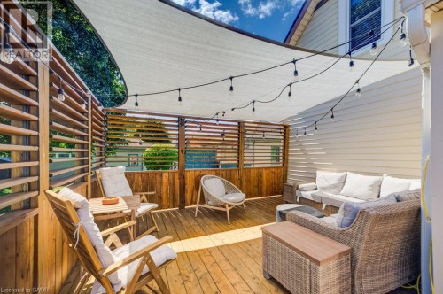 Expansive outdoor deck featuring wood flooring, slatted wood privacy screens, overhead string lighting, and a partial shade canopy - 209 Belleview Avenue, Kitchener, ON - Outdoor With Deck Patio Veranda With Exterior
