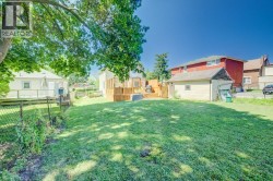 Spacious rear yard featuring an expansive lawn, mature shade trees, a raised wood deck, and an additional detached structure - 