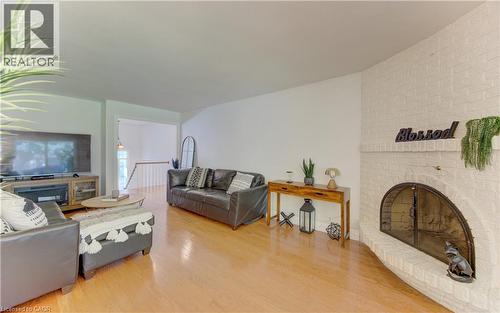 Living area featuring a painted brick corner fireplace with an arched firebox, light wood-finish flooring, and white walls - 106 Autumn Hill Crescent, Kitchener, ON - Indoor Photo Showing Living Room With Fireplace