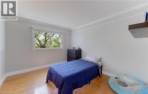 Light-filled room featuring wood-finish flooring, white crown molding, a large window with natural light, and a built-in floating shelf - 106 Autumn Hill Crescent, Kitchener, ON - Indoor Photo Showing Bedroom