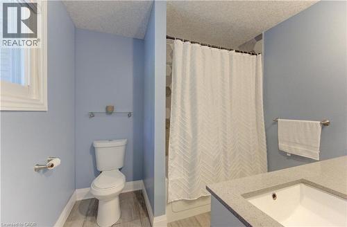 Contemporary bathroom featuring a window, wood-finish flooring, a white toilet, and a vanity with an integrated sink and light-toned countertop - 106 Autumn Hill Crescent, Kitchener, ON - Indoor Photo Showing Bathroom